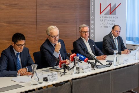 Vier Männer sitzen auf einem Tisch im Rahmen einer Pressekonferenz.