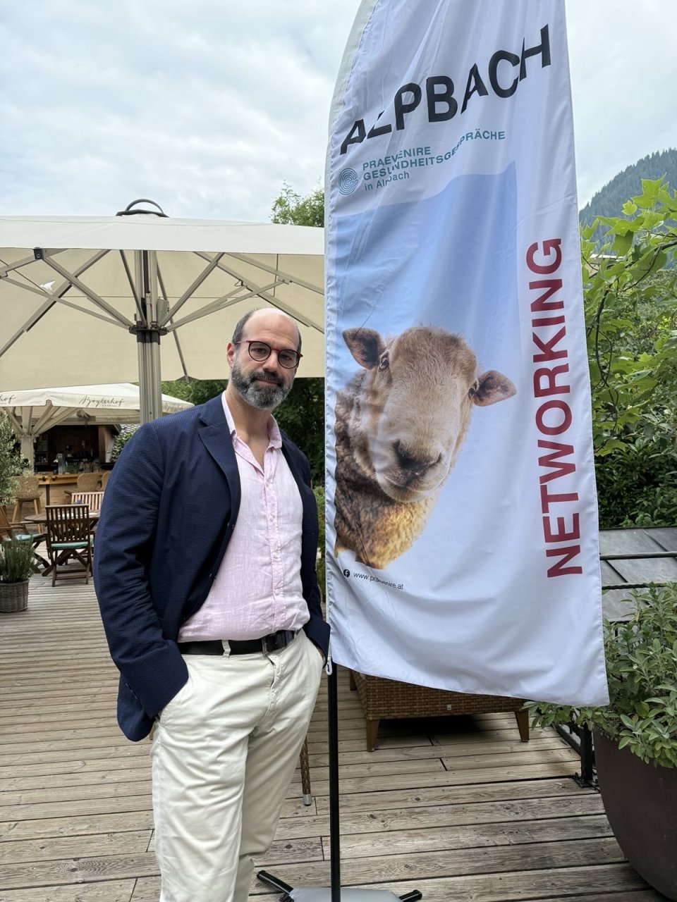 Matthias Brenner, Referent in der Kammer für Ärztinnen und Ärzte in Wien steht im Rahmen des Alpbach-Forums auf einer Terrasse neben einem Plakat auf dem "Networking" steht.