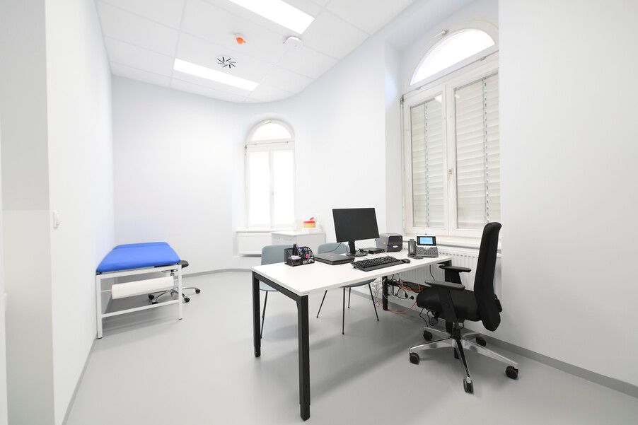 Die sehr nüchtern gehaltenen Räumlichkeiten der Wiener Gewaltambulanz - mit einem Schreibtisch, hellen Wänden, eine Patienten-Liege auf der linken Seite und viel Licht. Die Fenster sind mit Jalousien zugezogen.