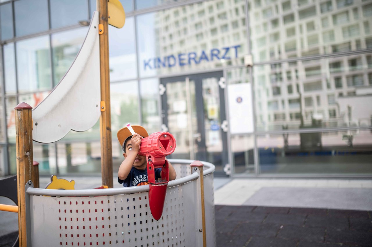 Ein Kind schaut auf einem kleinen Spielplatz vor einer Kinderarzt-Ordination auf einem nachgestellten Piratenschiff durch ein Fernrohr.