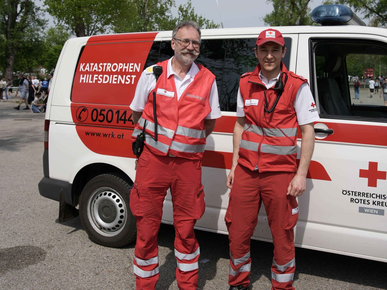 Zwei Mitarbeiter des Roten Kreuzes stehen bei einem Einsatzfahrzeug entlang der Rennstrecke.