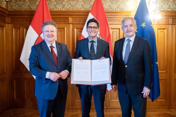 Drei Männer, von denen einer eine Urkunde in die Kamera hält. 