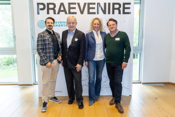 Drei Männer und eine Frau vor einer Logo-Wand stehend.