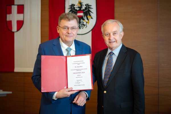 Zwei Männer, von denen einer eine Urkunde in die Kamera hält. 