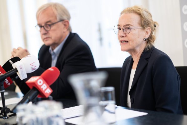 Zwei Personen an einem Tisch vor Mikrofonen sitzend.