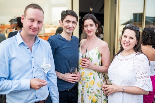 Gruppe von insgesamt vier Personen - zwei Männern und zwei Frauen - auf der Terrasse stehend mit Getränken in der Hand.