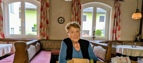 Maria Hengstberger sitzt auf einem Sessel an einem Tisch. Vor ihr, am Tisch, steht ihr Schutzhaus-Modell