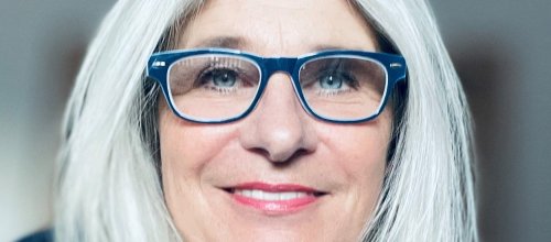 Frau mit Brille lächelt in die Kamera. 