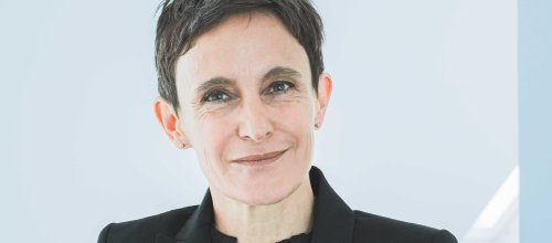 Frau im Blazer lächelt in die Kamera.