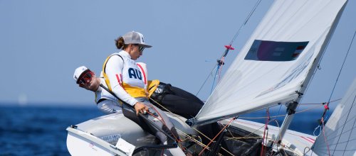 Zwei Personen, eine Frau und ein Mann, an Bord eines Segelboots, das sich im Wind stark neigt.
