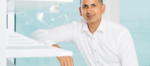 Der Mediziner Wali Malik sitzt in einem Labor, weiß bekleidet und blickt direkt in die Kamera.
