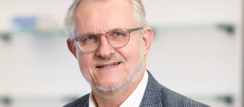 Mann mit Brille, Hemd und Sakko lächelt in die Kamera.