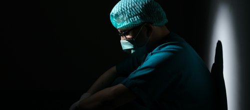 Mann in OP-Kleidung sitzt nachdenklich im Dunkeln