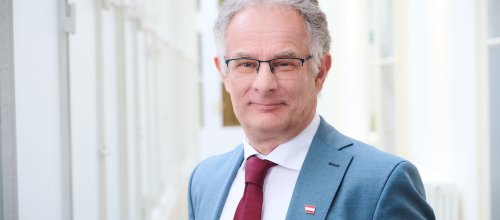 Mann im Sakko mit grauen Haaren und Brille. 