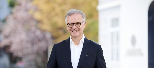 Mann in Anzug steht lächelnd vor Gebäude
