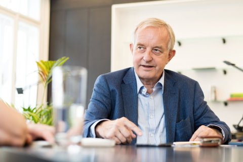 Präsident Johannes Steinhart sitzt an einem Tisch während eines Interviews und sieht dabei die Interviewerin an, von der man aber nur die Hand sehen kann.