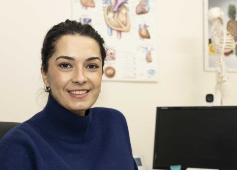 Auf dem Foto ist die junge Ärztin Shirin Johari zu sehen, die eine dunkelvioletten Rollkragen-Pullover trägt - im Hintergrund sieht man ein medizinisches Plakat und daneben steht ein künstliches Skelett, was darauf schließen lässt, dass man in einer ärztlichen Ordination ist.