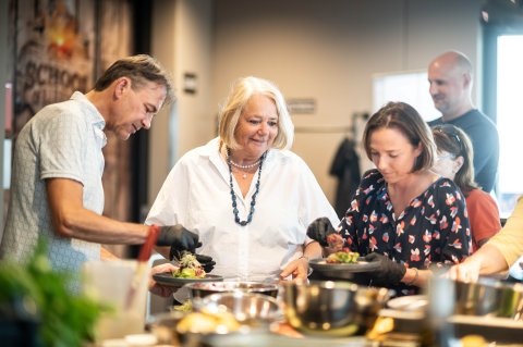 Ein Mann und zwei Frauen stehen an einem Herd und bereiten Speisen zu.