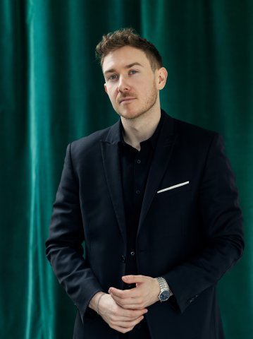 Eine Porträtaufnahme von Zukunftsforscher Tristan Horx - der ein dunkles Gewand trägt und im Hintergrund einen smaragdgrünen Vorhang hat.