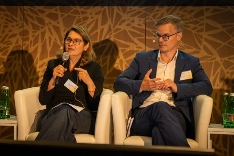 Eine Frau und ein Mann sitzen auf einem Podium einer Diskussionsrunde.