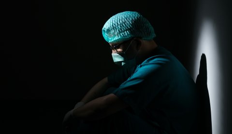 Mann in OP-Kleidung sitzt nachdenklich im Dunkeln