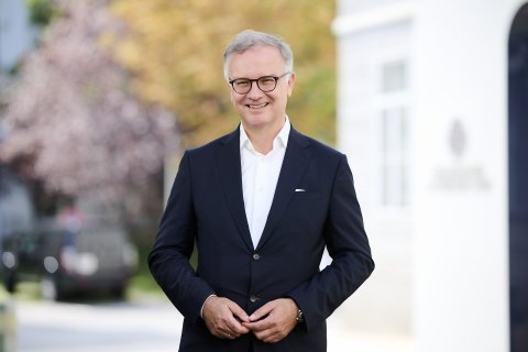 Mann in Anzug steht lächelnd vor Gebäude