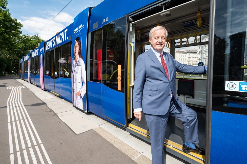 Ein steht in der Tür einer geöffneten Straßenbahn - mit einem Bein noch in der Straßenbahn, mit dem anderen bereits am Trottoir.