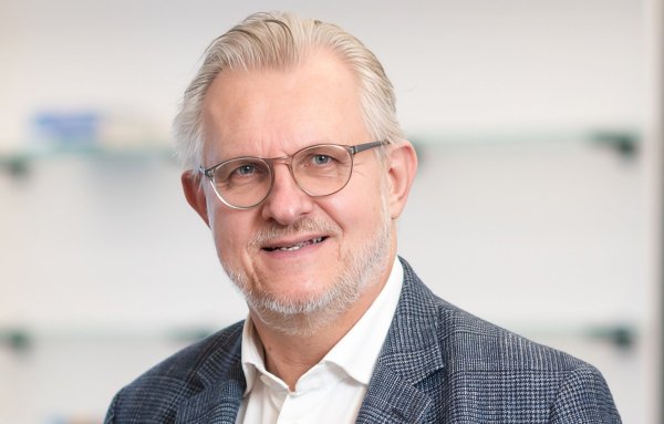 Mann mit Brille, Hemd und Sakko lächelt in die Kamera.