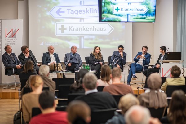 Wilhelm Marhold, Herwig Ostermann, Jan Pazourek, Richard Gauss, Naghme Kamaleyan-Schmied, Eduardo Maldonado-González, Benjamin Glaser und Moderator Köksal Baltaci (v.l.) sitzen nebeneinander auf dem Podium.
