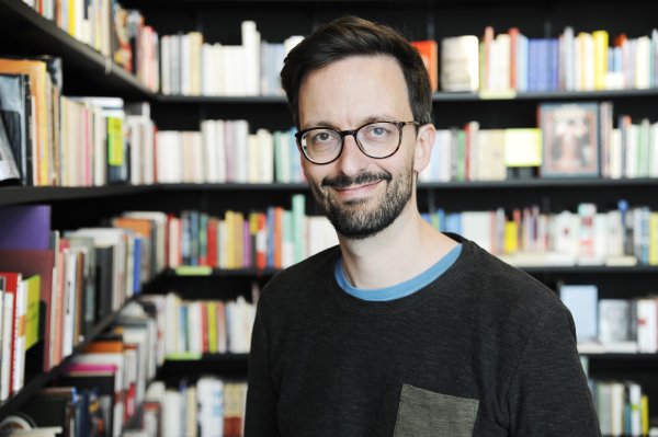 Mann mit Brille steht vor Bücherwand 
