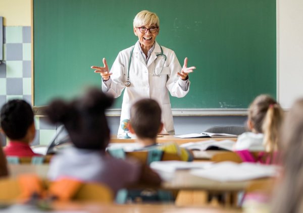 Eine Ärztin steht im Klassenzimmer und unterrichtet Gesundheit.